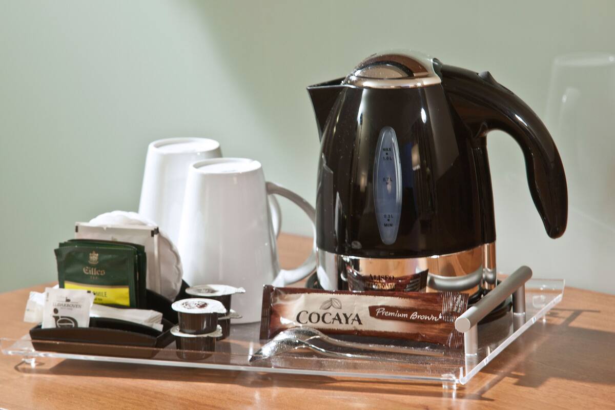 A coffee maker, a set of white cups, a tea set, and a COCAYA chocolate bar on a clear tray.