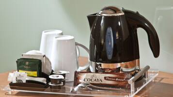 A coffee maker, a set of white cups, a tea set, and a COCAYA chocolate bar on a clear tray.
