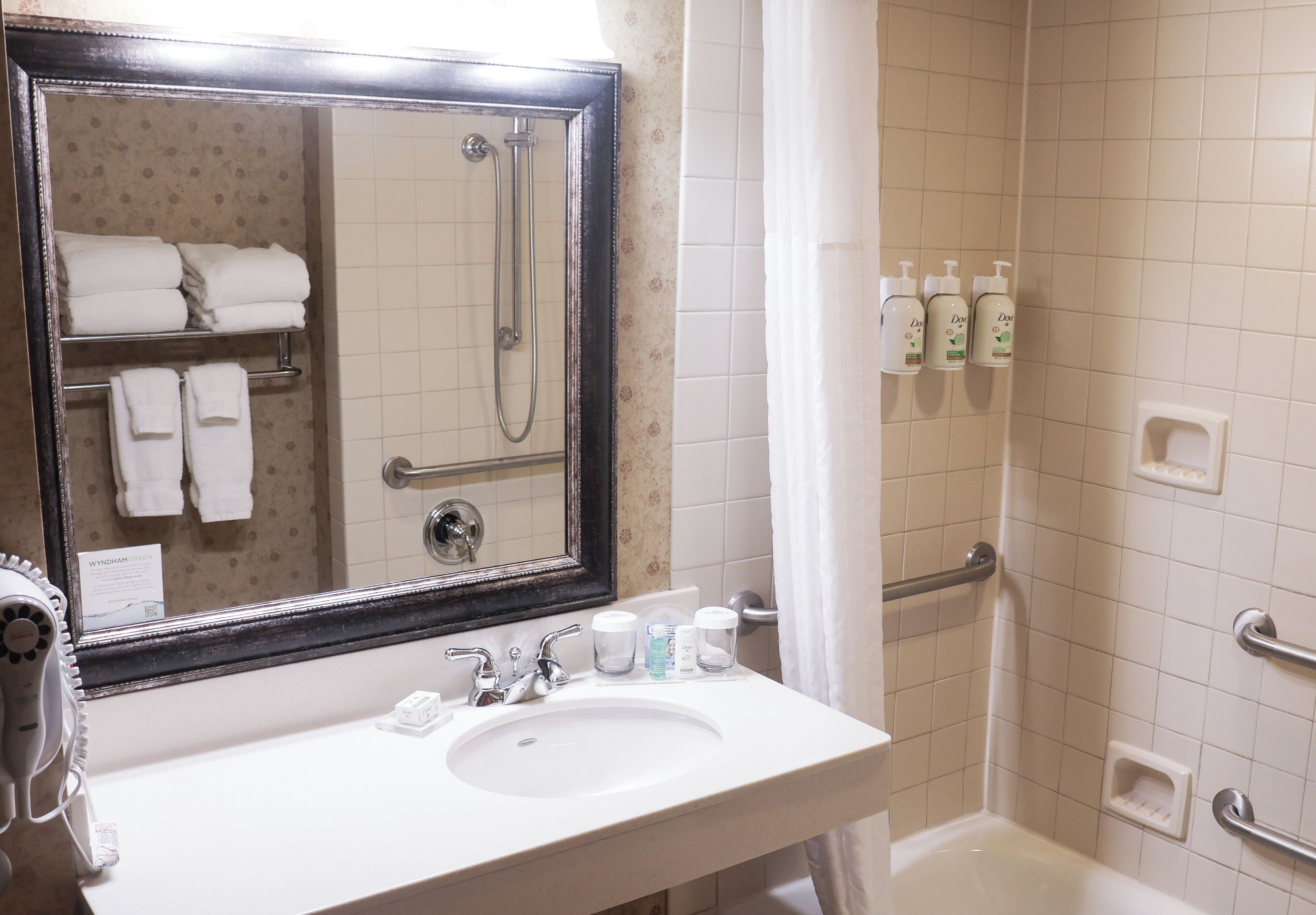 A bathroom with a white sink, a large mirror, a shower with a glass door, and toiletries on the wall.