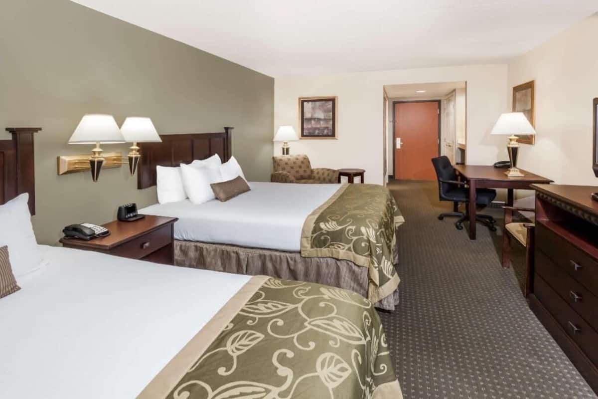 Une chambre d’hôtel avec deux lits, un bureau, une chaise, un téléphone et une lampe.