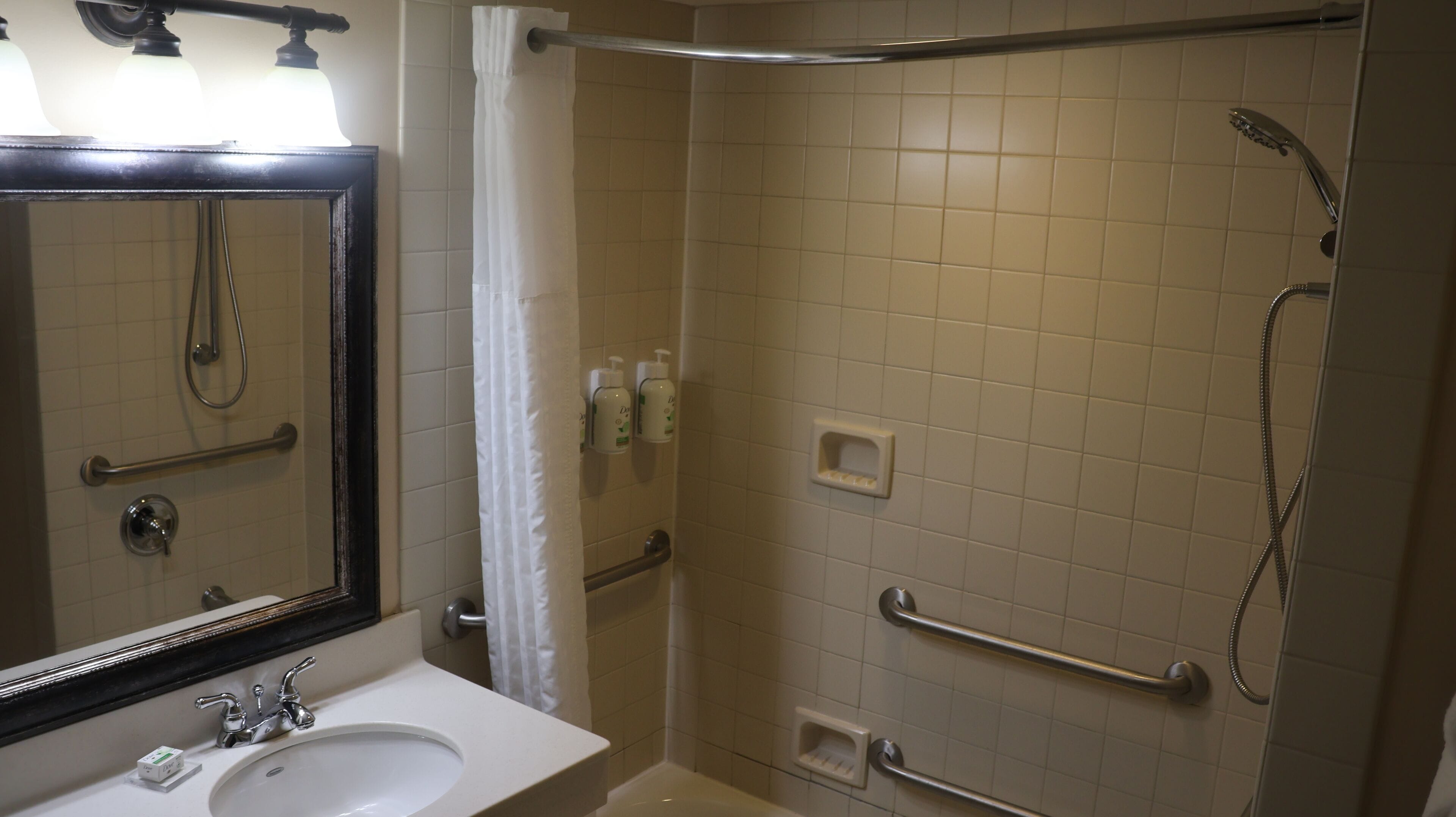 A bathroom with a sink, mirror, shower, and grab bars.