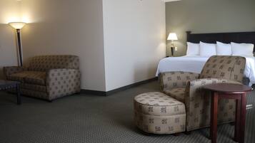 A hotel room with a bed, two armchairs, a small table, and a nightstand with lamps.
