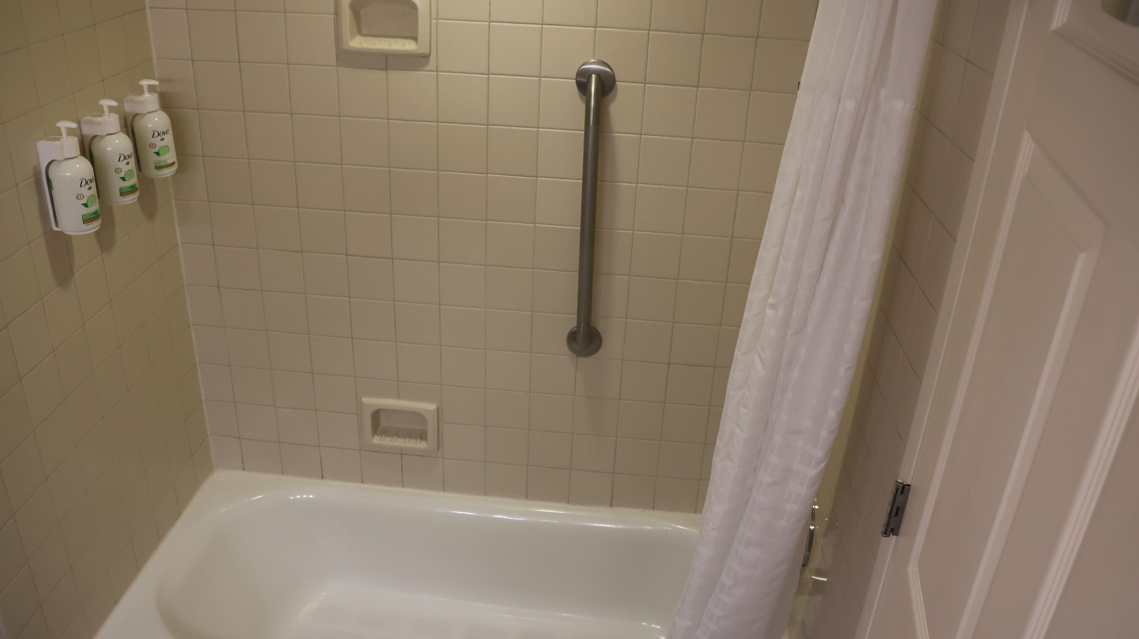 Ein Badezimmer mit einer Badewanne, einer Haltestange und drei Dove Handseifenspendern an der Wand.