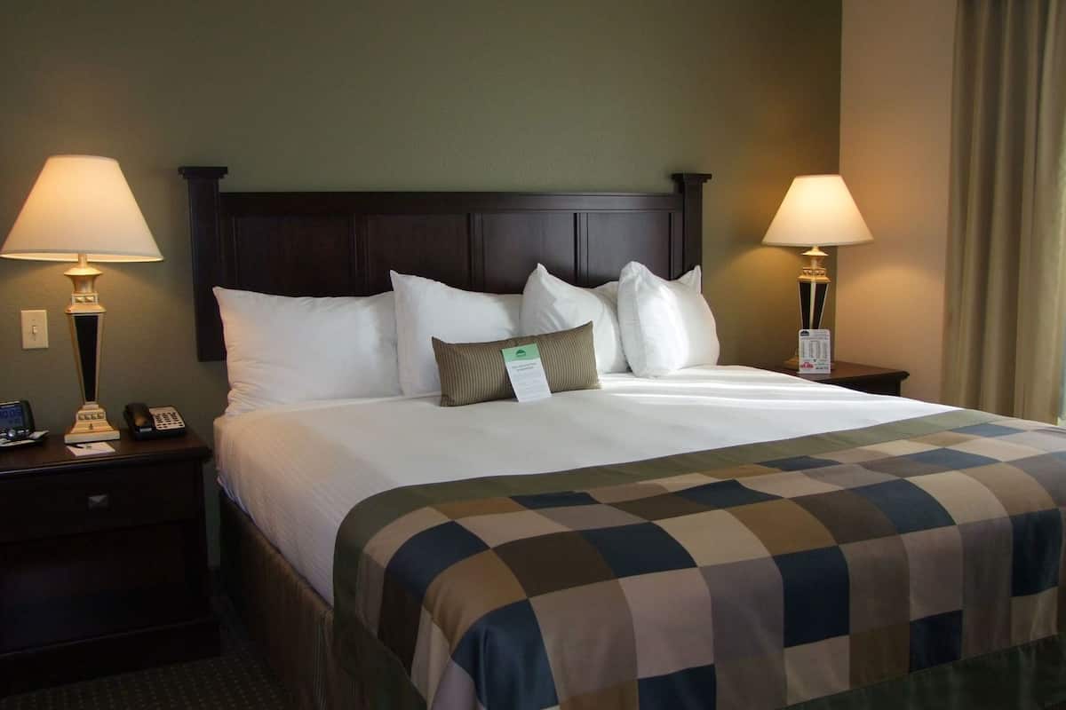Une chambre d’hôtel avec un grand lit, deux tables de chevet avec des lampes, une petite table avec un téléphone et une carte d’enregistrement posée sur le lit.