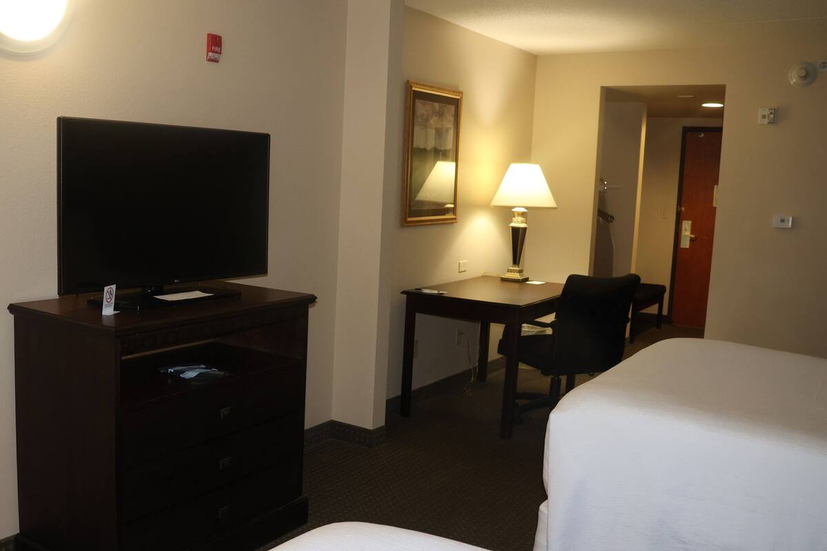 Une chambre d’hôtel équipée d’un téléviseur à écran plat posé sur une commode, d’un bureau avec une lampe, de deux lits simples et d’une porte donnant sur une autre pièce.
