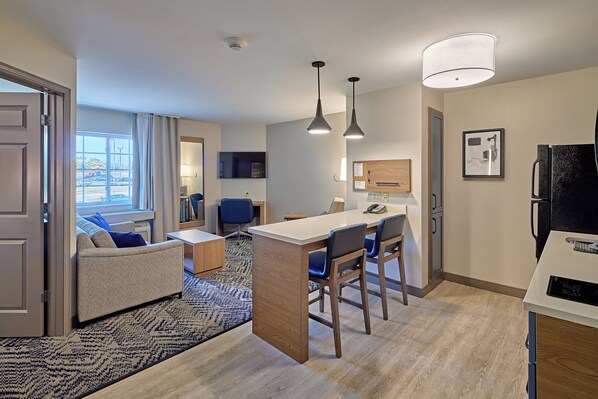 A modern kitchen with a central island, bar stools, pendant lighting, and a view of the outdoors through large windows.