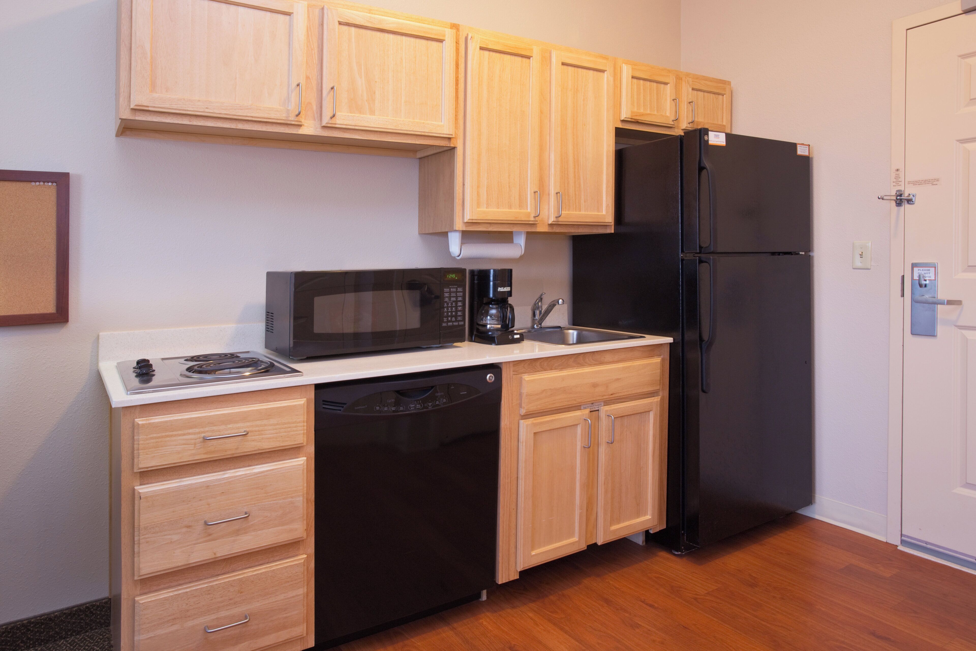A compact kitchen with wooden cabinets, a black refrigerator, a microwave, and a dishwasher.