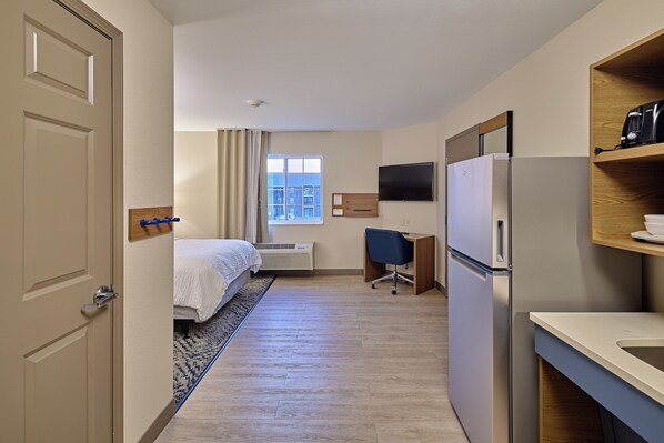 A hotel room with a bed, desk, refrigerator, and a view of the city through the window.