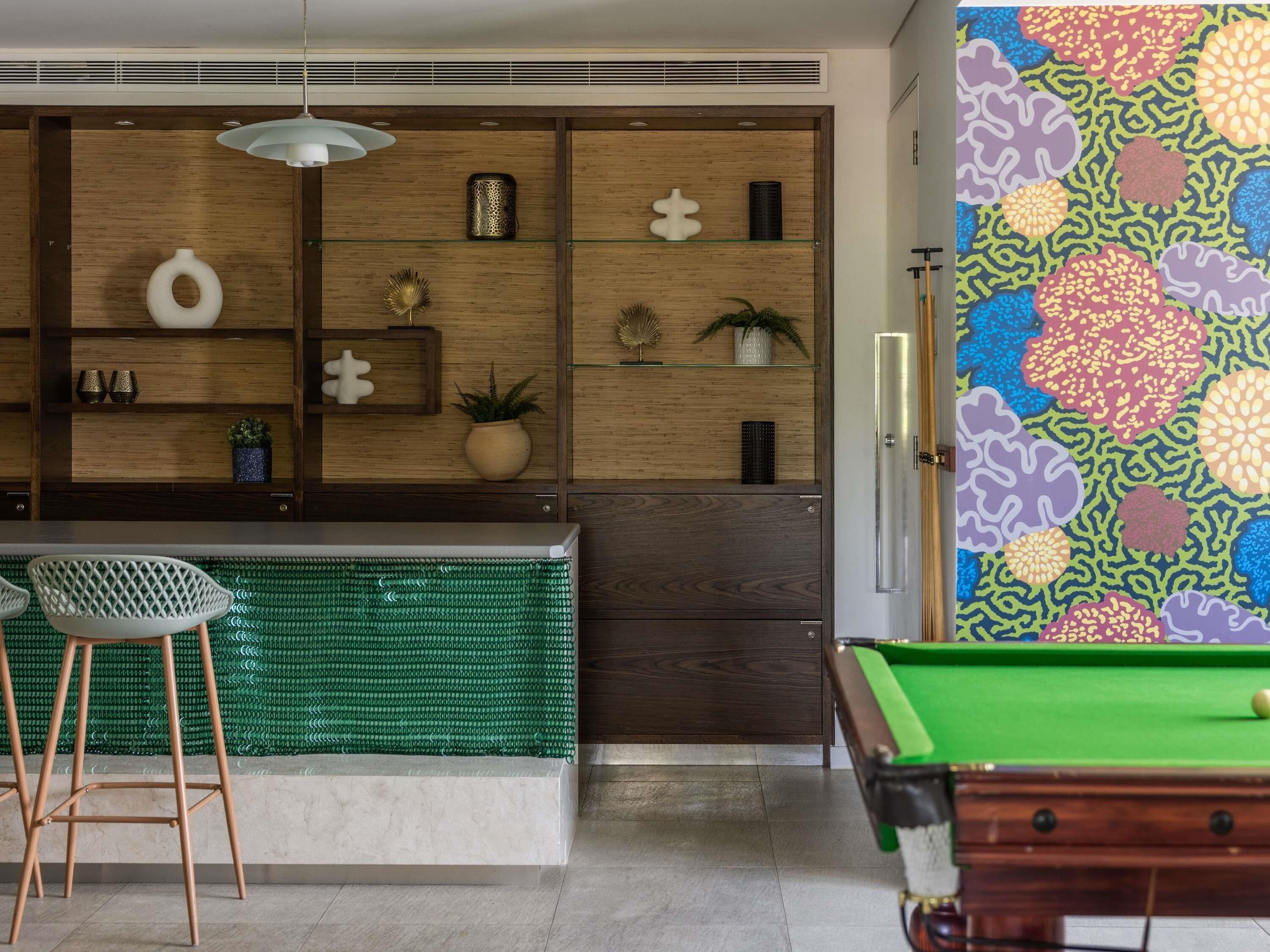 A pool table, a bar area with stools, and a decorative wall.