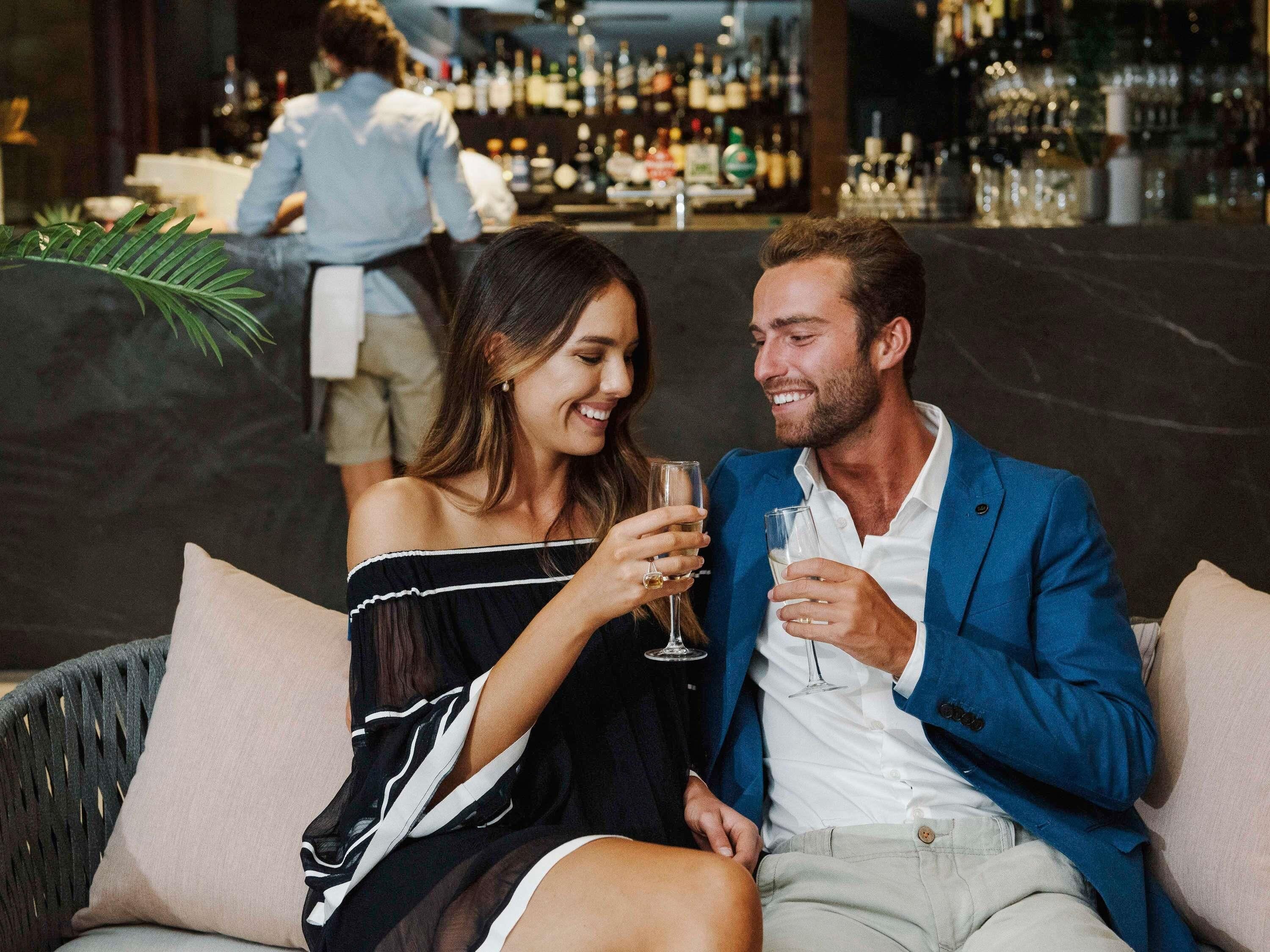 Una pareja sentada en un sofá de mimbre con un bar al fondo.