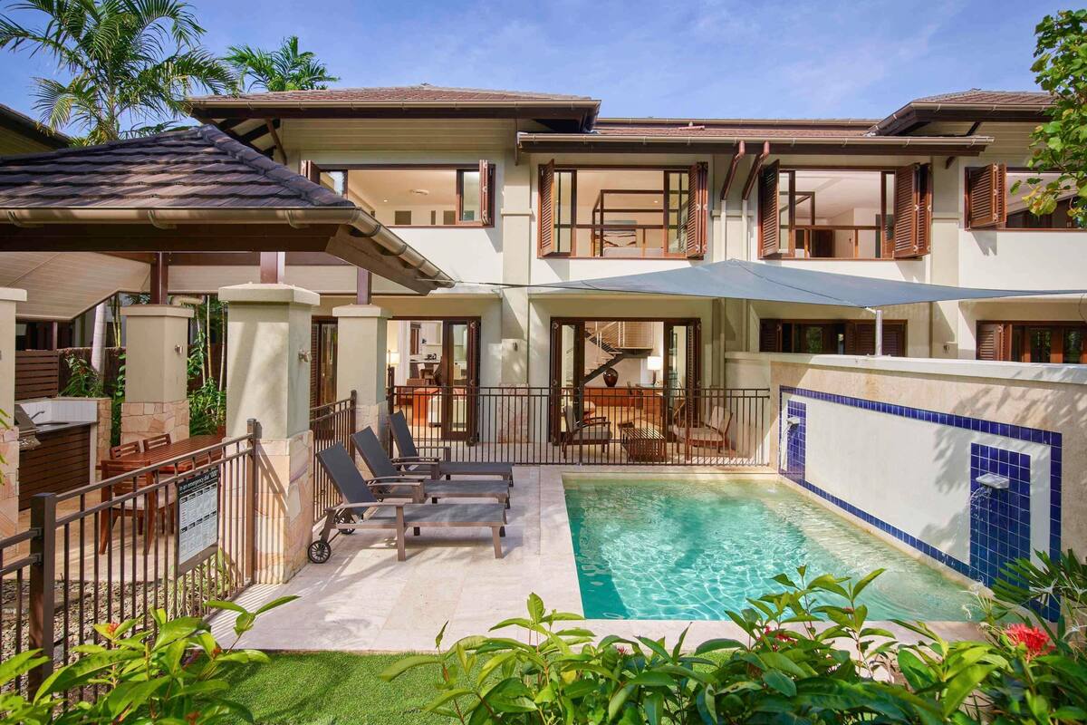 Une maison à deux étages dotée d’une piscine, d’un espace salon extérieur et d’un patio couvert.