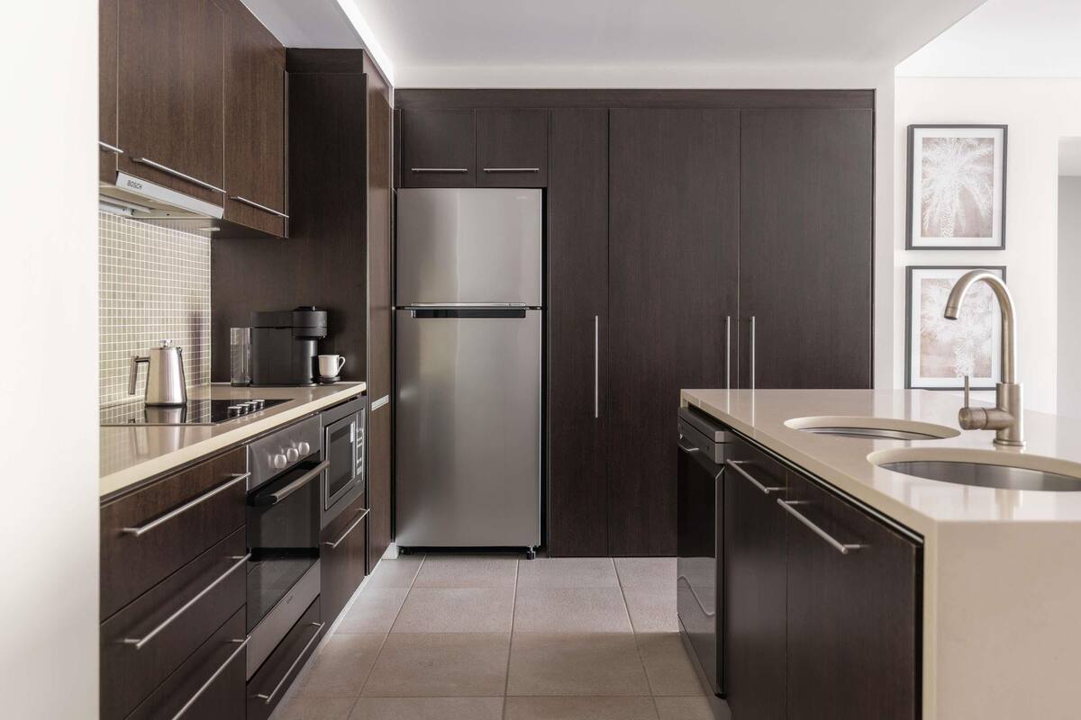 Une cuisine moderne avec des meubles en bois foncé, des appareils électroménagers en acier inoxydable et un évier à deux bacs.
