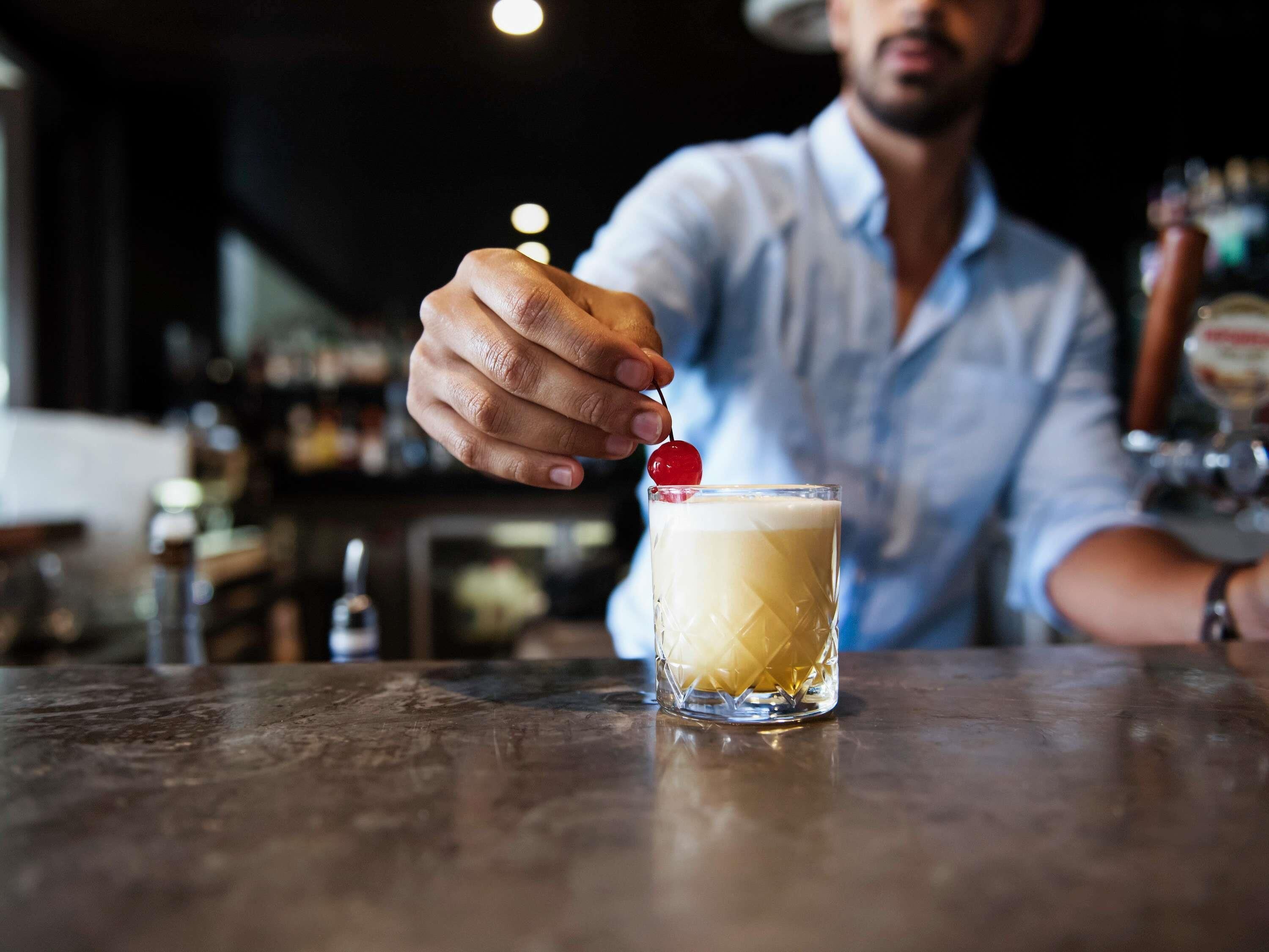 A person serving a cocktail with a cherry garnish.