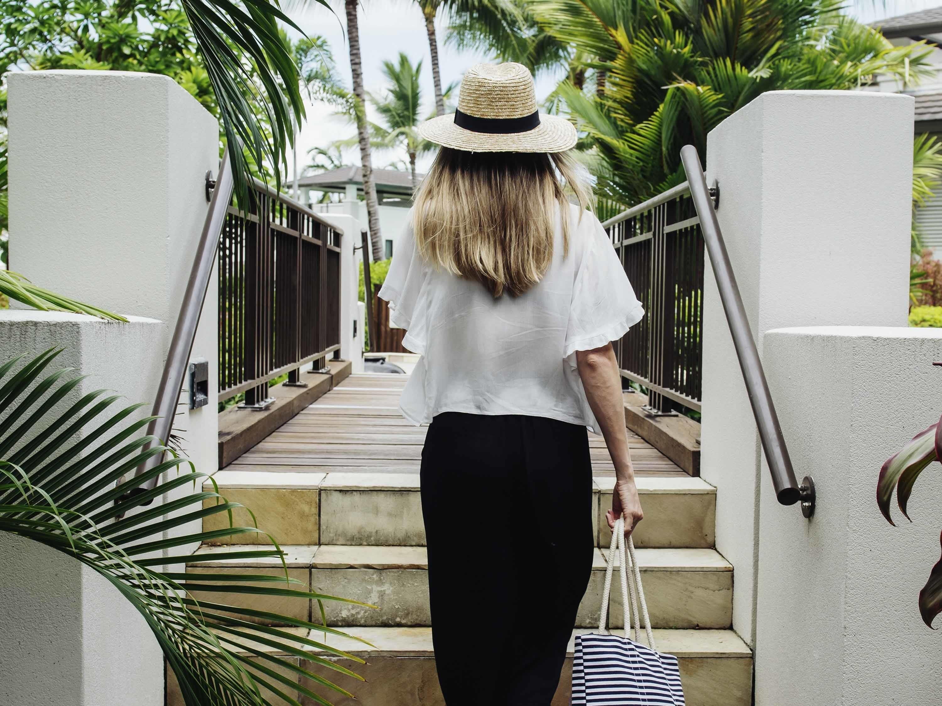 A person descending a wooden staircase with metal railings, surrounded by lush greenery and palm trees.