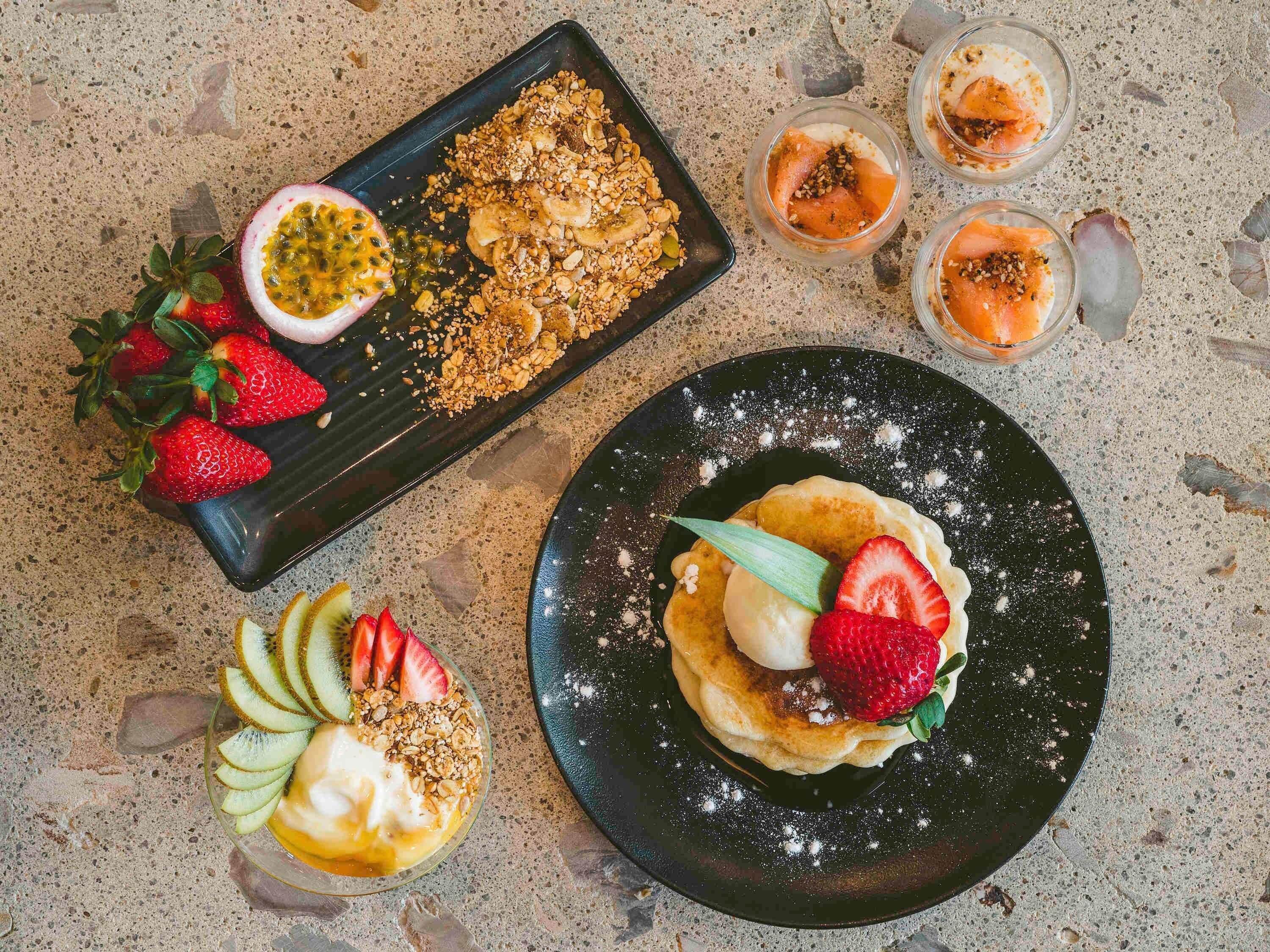 Een dessertbord met pannenkoeken, aardbeien en een passievrucht.