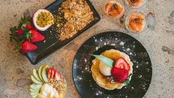 Een dessertbord met pannenkoeken, aardbeien en een passievrucht.