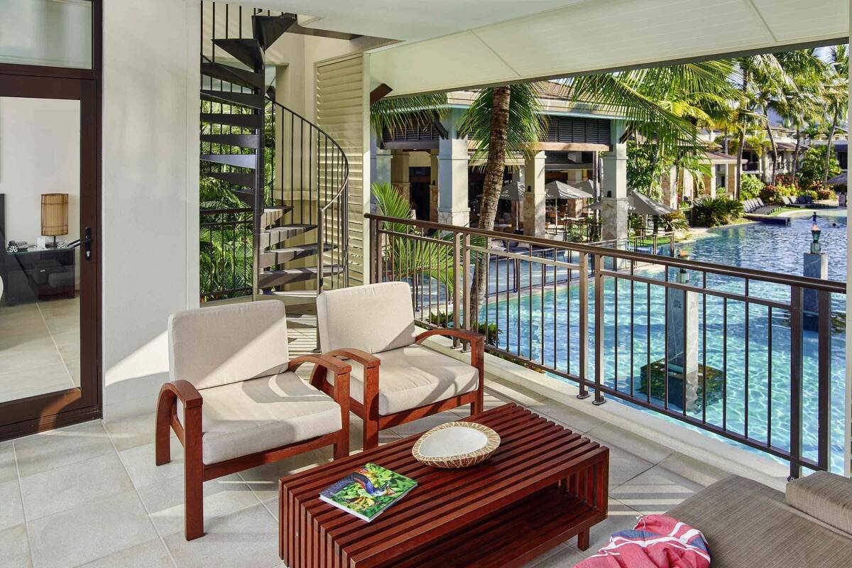 Un balcon avec vue sur la piscine, des meubles en bois et un escalier.