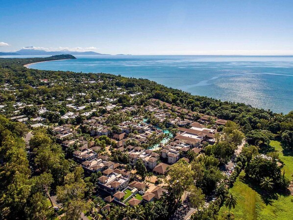 Vue aérienne d’un quartier résidentiel situé sur la côte, avec des maisons, une piscine et une plage.