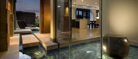 A modern interior with a glass-enclosed water feature, stone steps, and a seating area with a view of the outdoors.