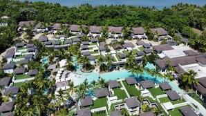 An aerial view of a resort with multiple bungalow-style buildings, a central swimming pool, and lush greenery surrounding the property.