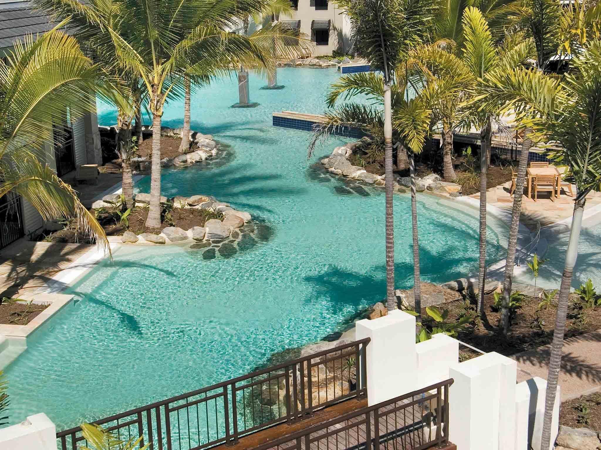 Zwembadgedeelte van een resort met helder water, omgeven door palmbomen en een pad van stenen.
