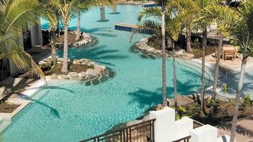 Zwembadgedeelte van een resort met helder water, omgeven door palmbomen en een pad van stenen.