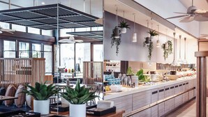 A modern kitchen with a long counter, hanging plants, and a ceiling fan.