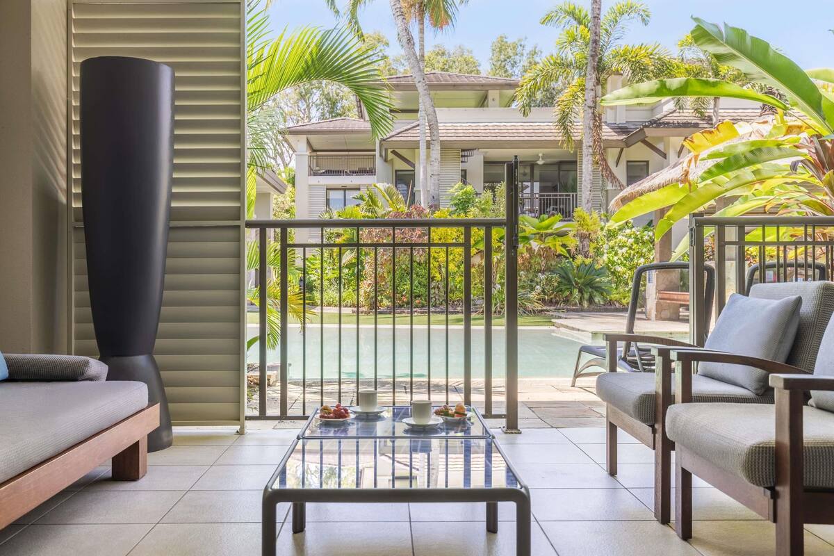 Un balcon donnant sur une piscine, des palmiers et un bâtiment avec un toit en tuiles.