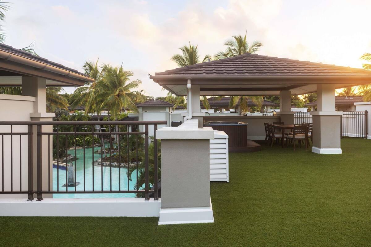 Un espace aménagé au bord de la piscine, comprenant un coin salon couvert, une piscine et une vue sur un complexe hôtelier.