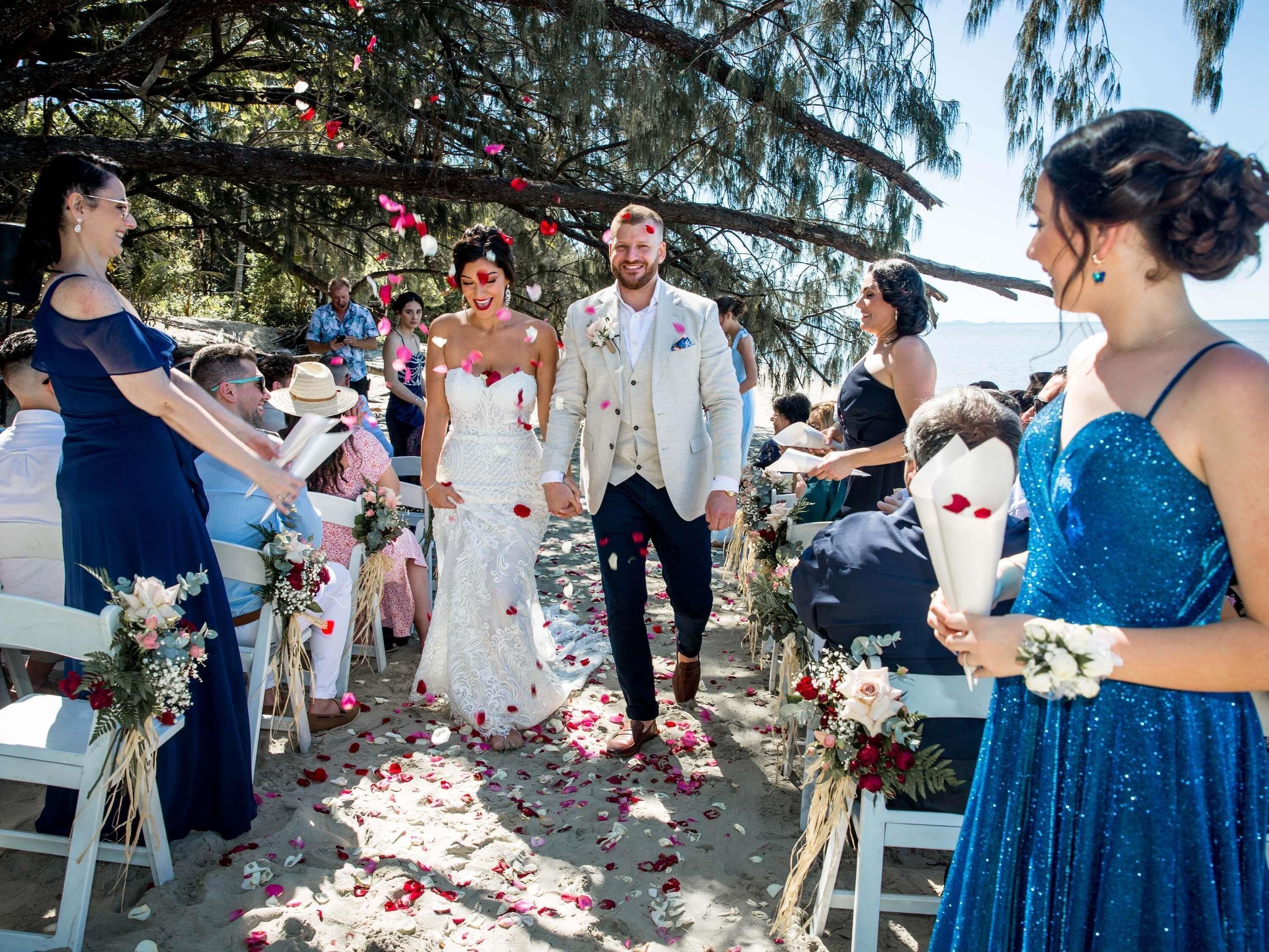 Una ceremonia de boda en la playa con sillas blancas y decoraciones florales.