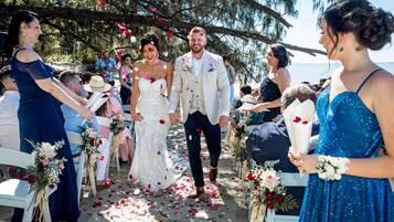 Una ceremonia de boda en la playa con sillas blancas y decoraciones florales.