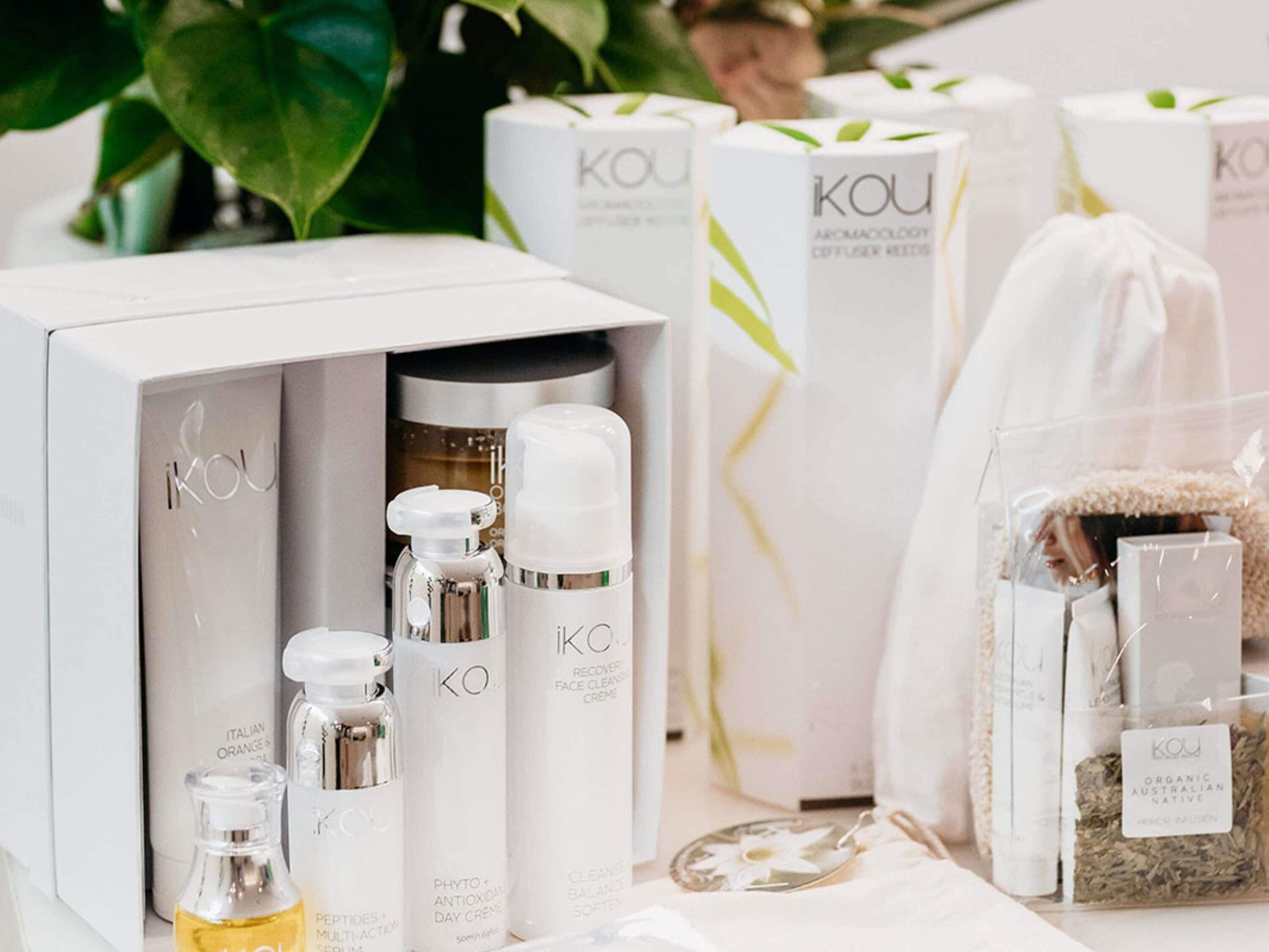 A variety of skincare products from the brand KOU, including a facial cleanser, serum, and a diffuser reed set.