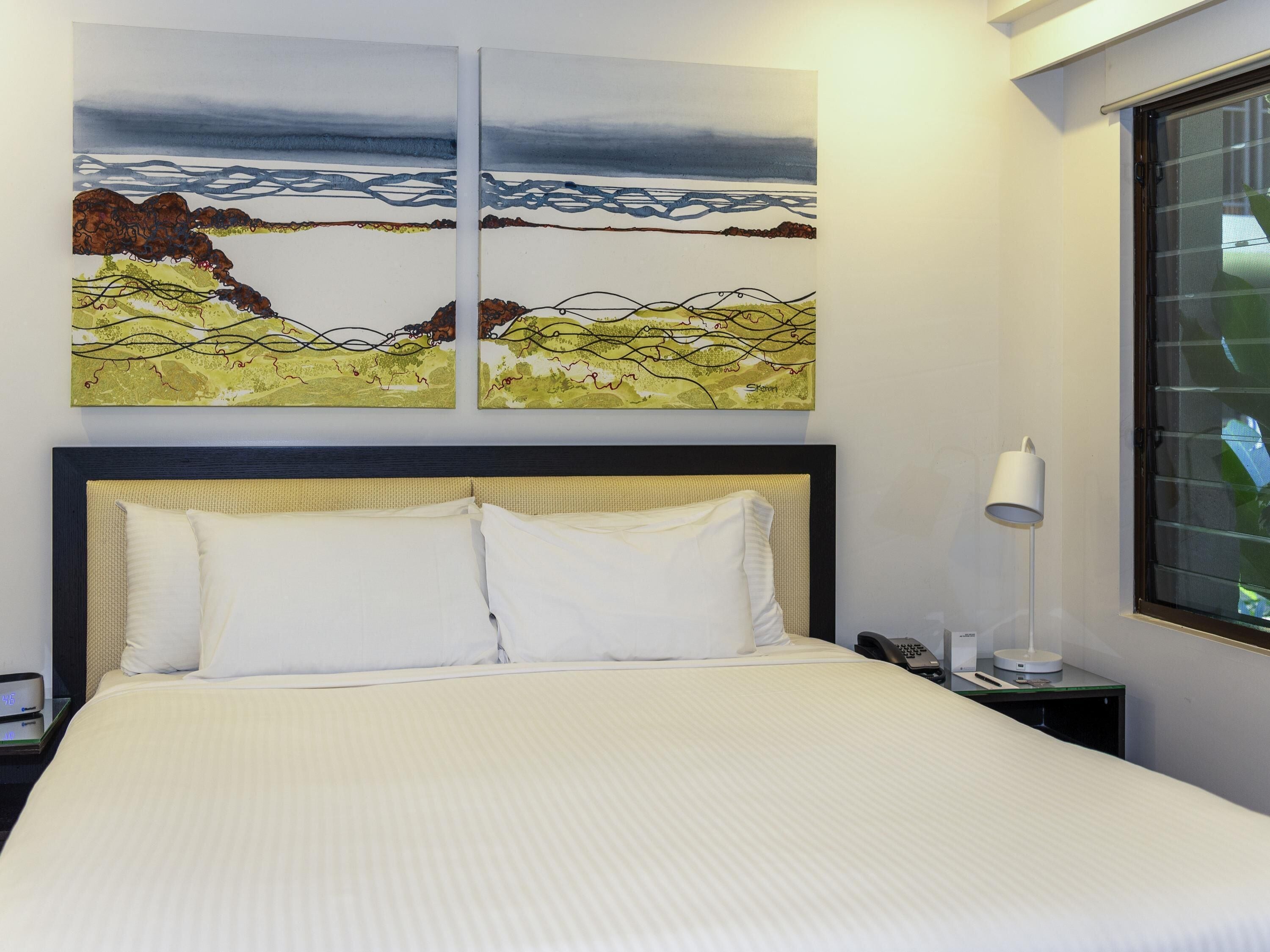 Une chambre d’hôtel avec un lit, une table de chevet avec une lampe et deux tableaux accrochés au mur.