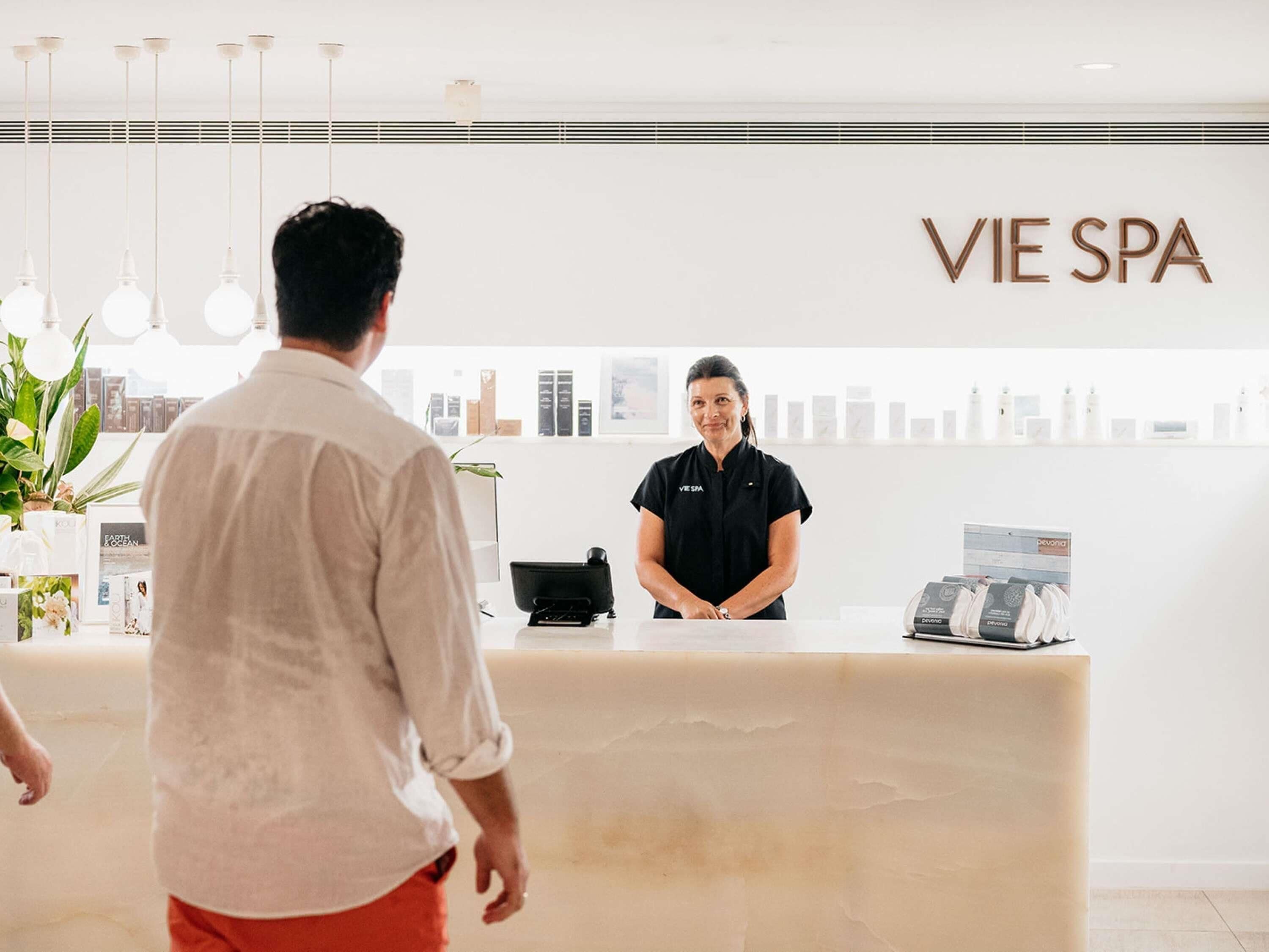 A reception desk with a sign reading 'VIE SPA' and a person standing behind it.