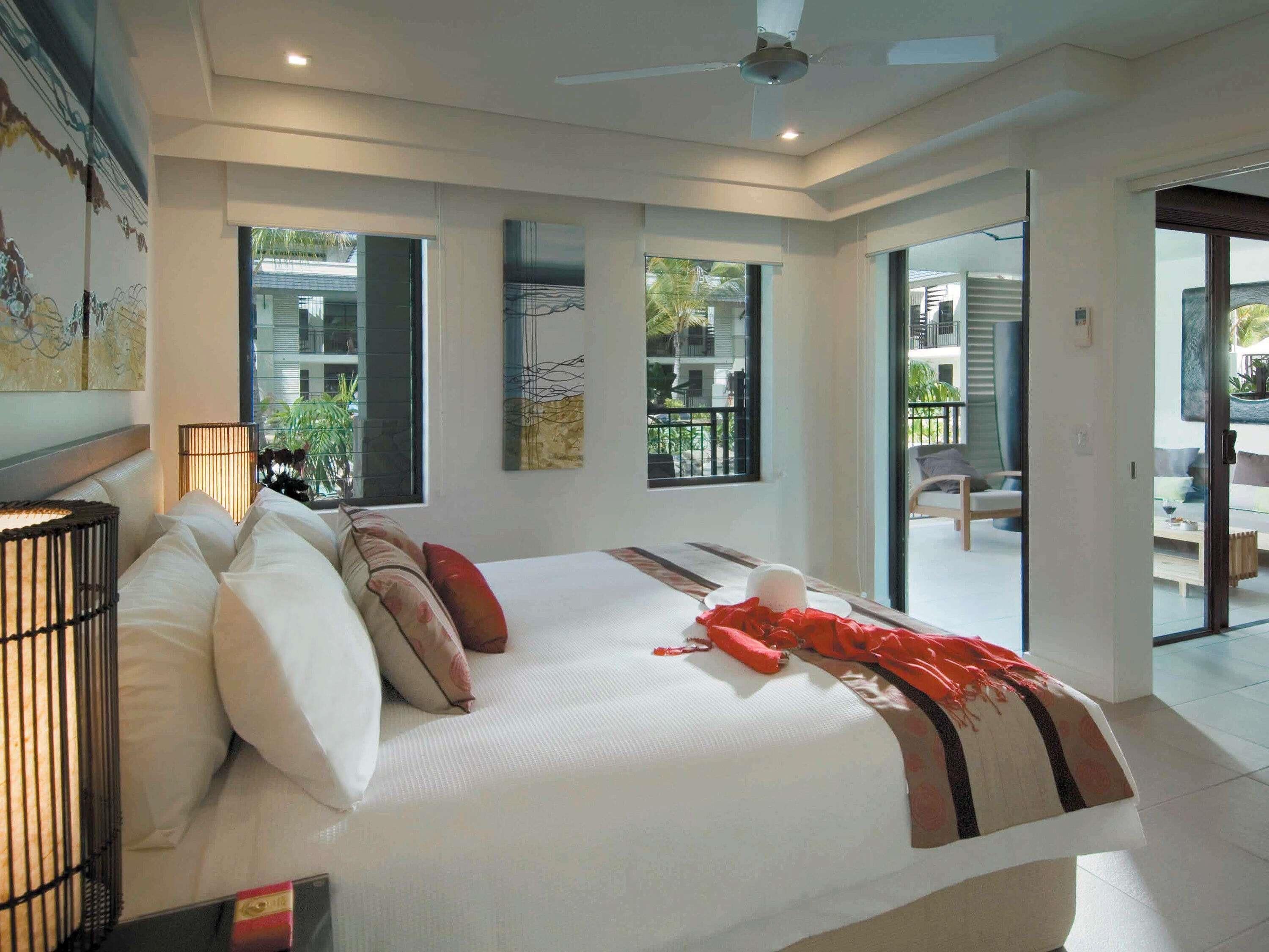Une chambre moderne avec un grand lit, un ventilateur de plafond et une vue sur le balcon extérieur.