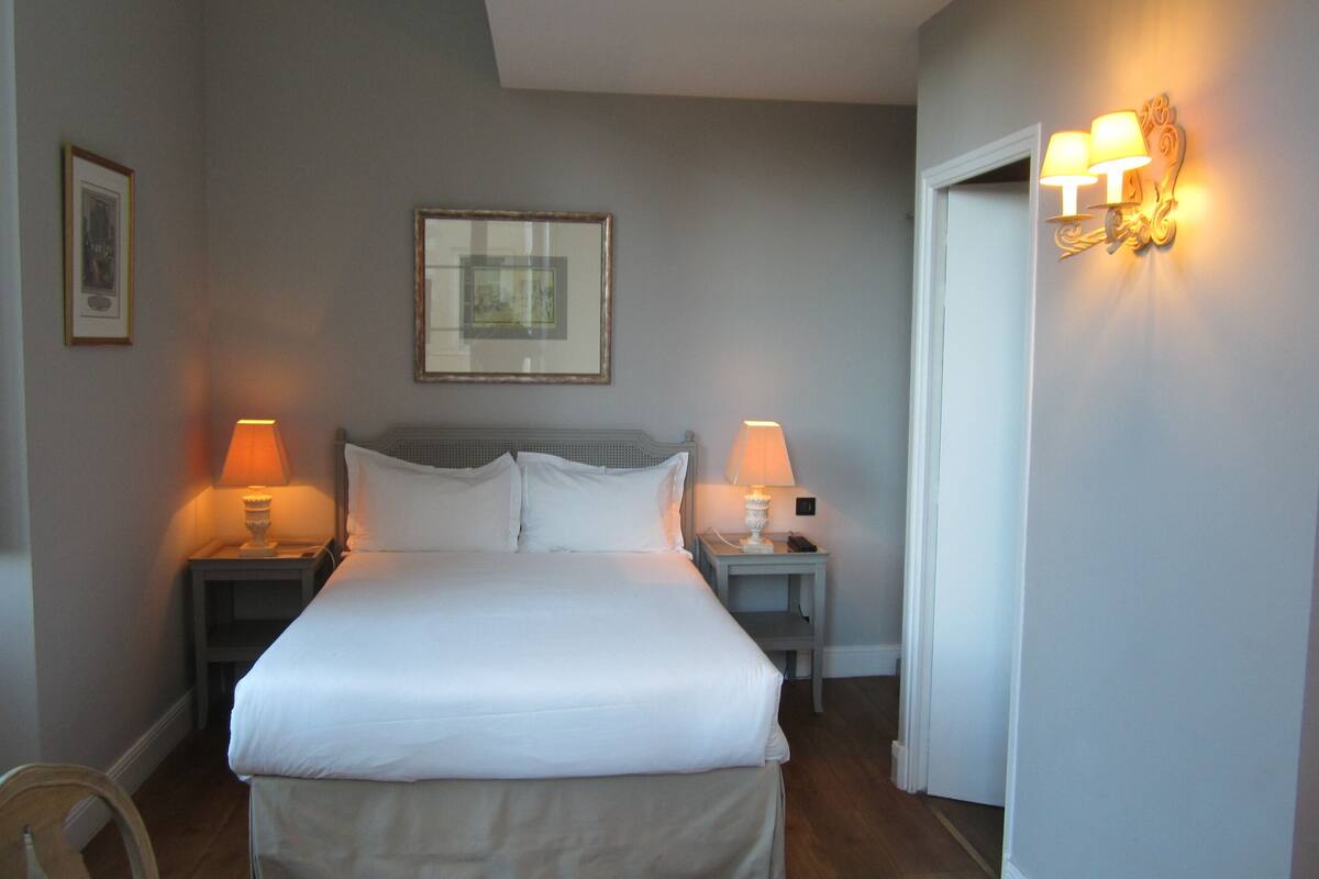 A neatly made bed with white linens, two bedside lamps, and a framed picture on the wall.