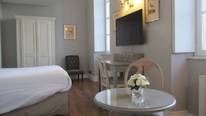 Un dormitorio con cama, una silla, una mesita con un florero, un escritorio y un televisor instalado en la pared.