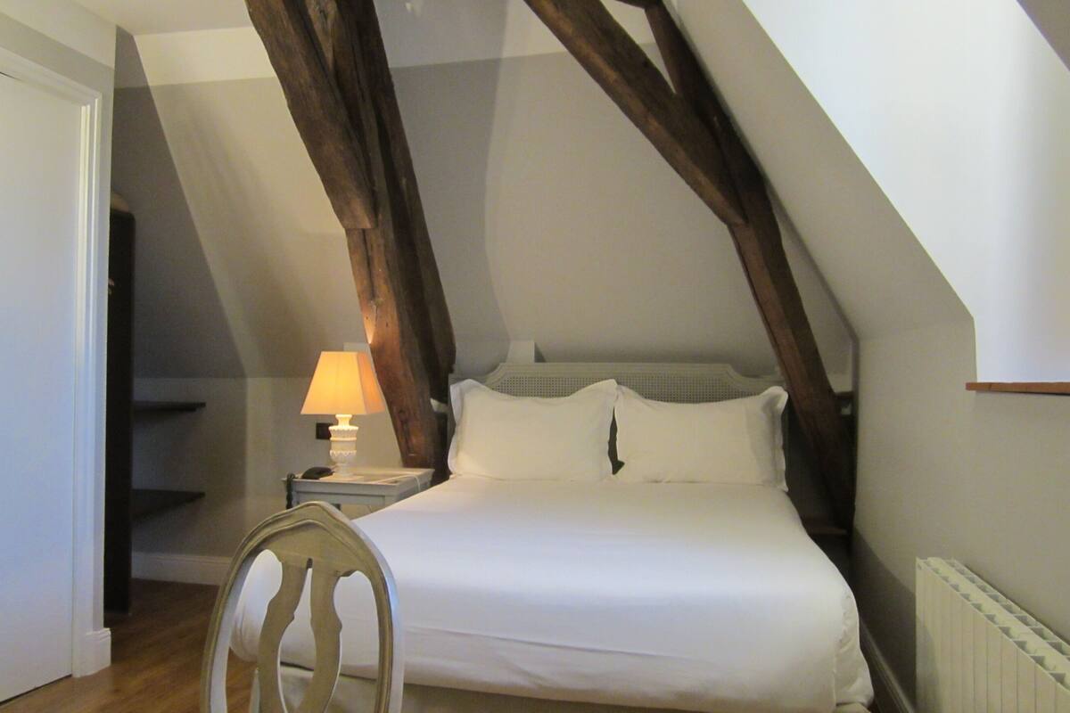 A bedroom with a bed, a nightstand, a lamp, and a chair.
