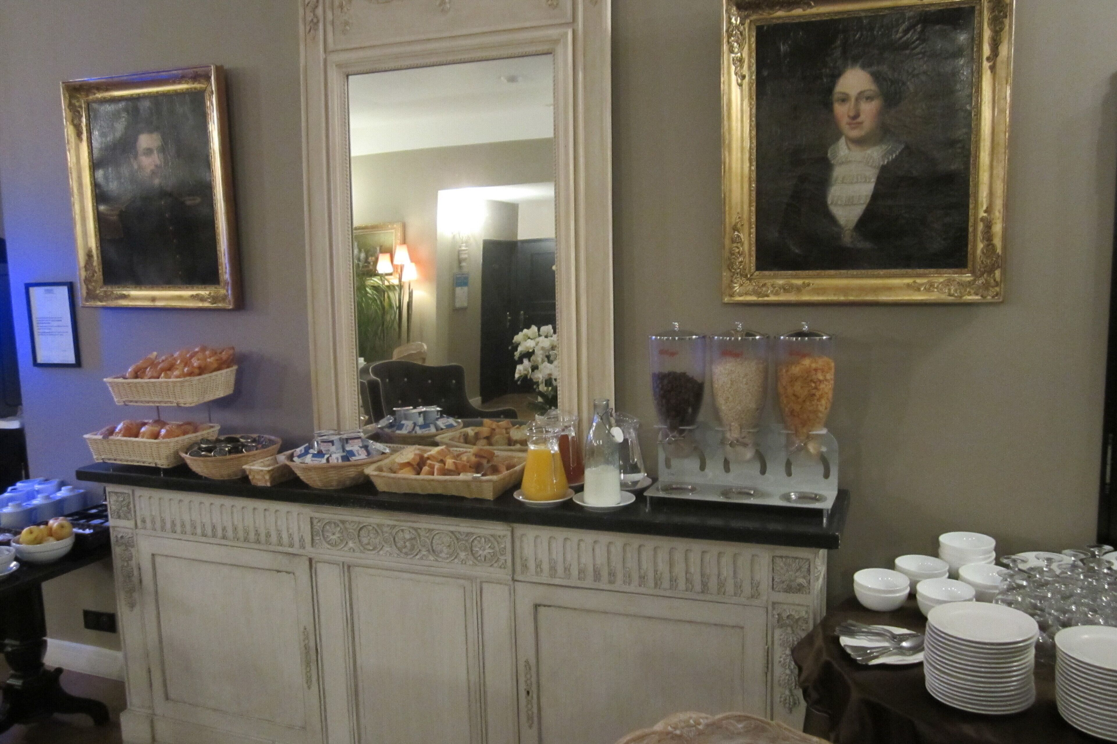 A buffet setup with various food items and beverages, including a fruit bowl, a juice dispenser, and a bread basket.