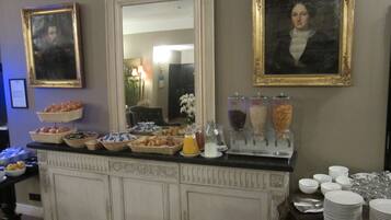 A buffet setup with various food items and beverages, including a fruit bowl, a juice dispenser, and a bread basket.