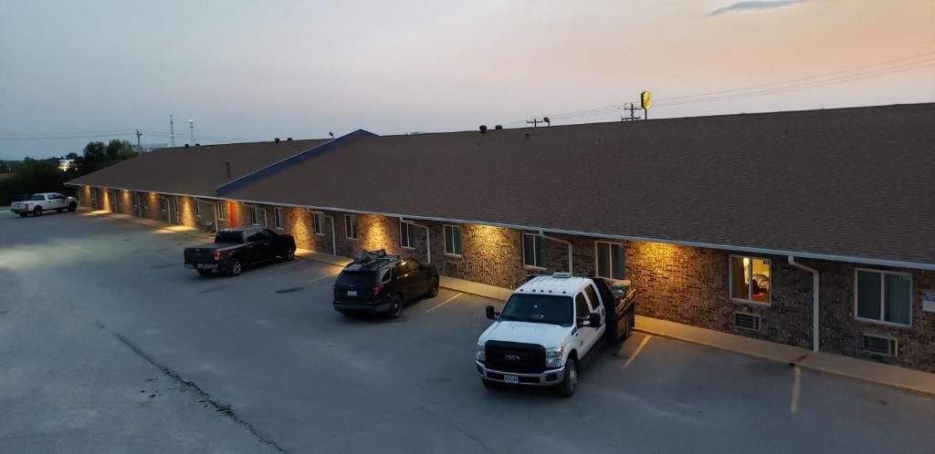 Un motel con una fila de habitaciones, un estacionamiento y un edificio de techo plano.