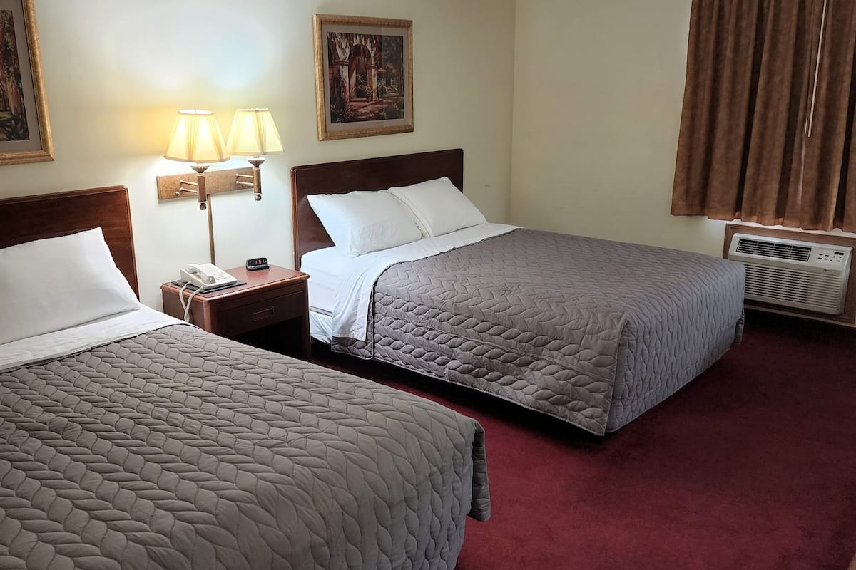 A hotel room with two beds, a nightstand with a lamp, a painting on the wall, and a window with curtains.