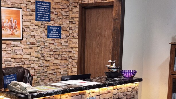 Un mostrador de recepción con un fondo de pared de piedra, una puerta de madera y un cartel que indica una posada económica para familias.