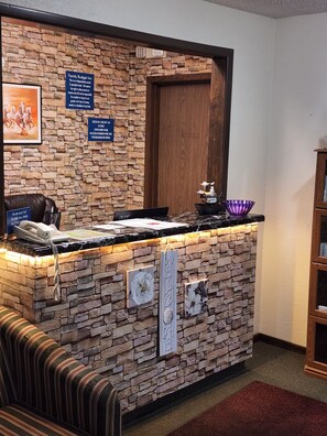 A reception desk with a stone wall backdrop, a wooden door, and a sign indicating a family budget inn. - Family Budget Inn Bethany (Bethany)