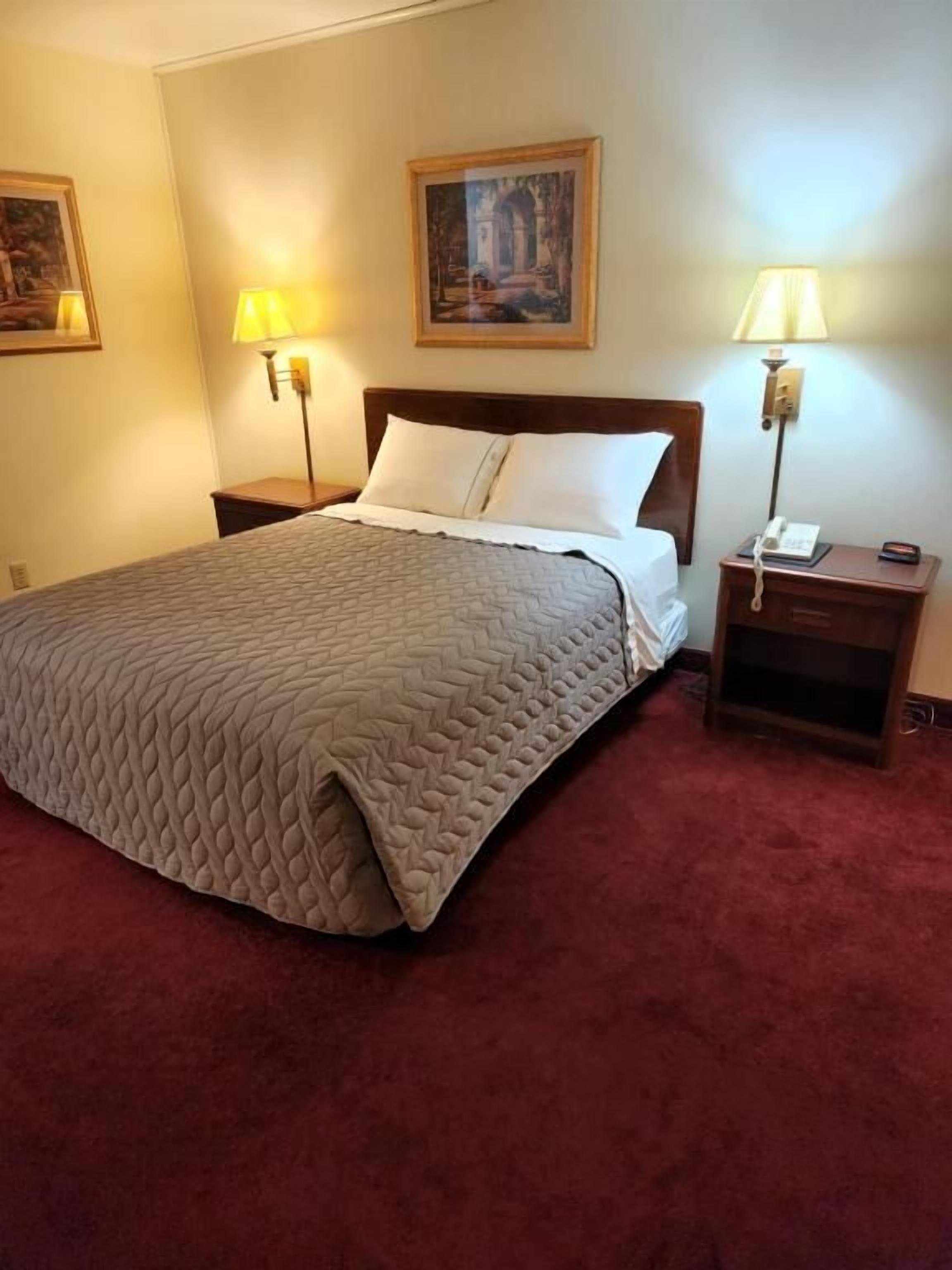 Une chambre d’hôtel avec un grand lit, deux tables de chevet, une petite table et deux lampes fixées au mur.