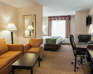 Quarto de hotel com sofá, poltrona, escrivaninha e cama com colcha verde.