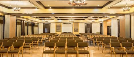 A conference room with rows of chairs, a stage, and chandeliers.