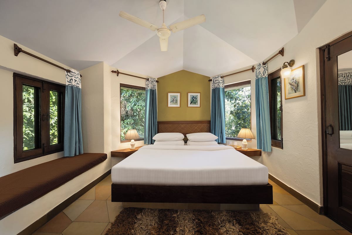 A bedroom with a large bed, two bedside tables with lamps, a ceiling fan, and a bench along the window sill.