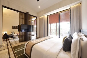 A hotel room with a large bed, a TV, a sofa, and a balcony with curtains.