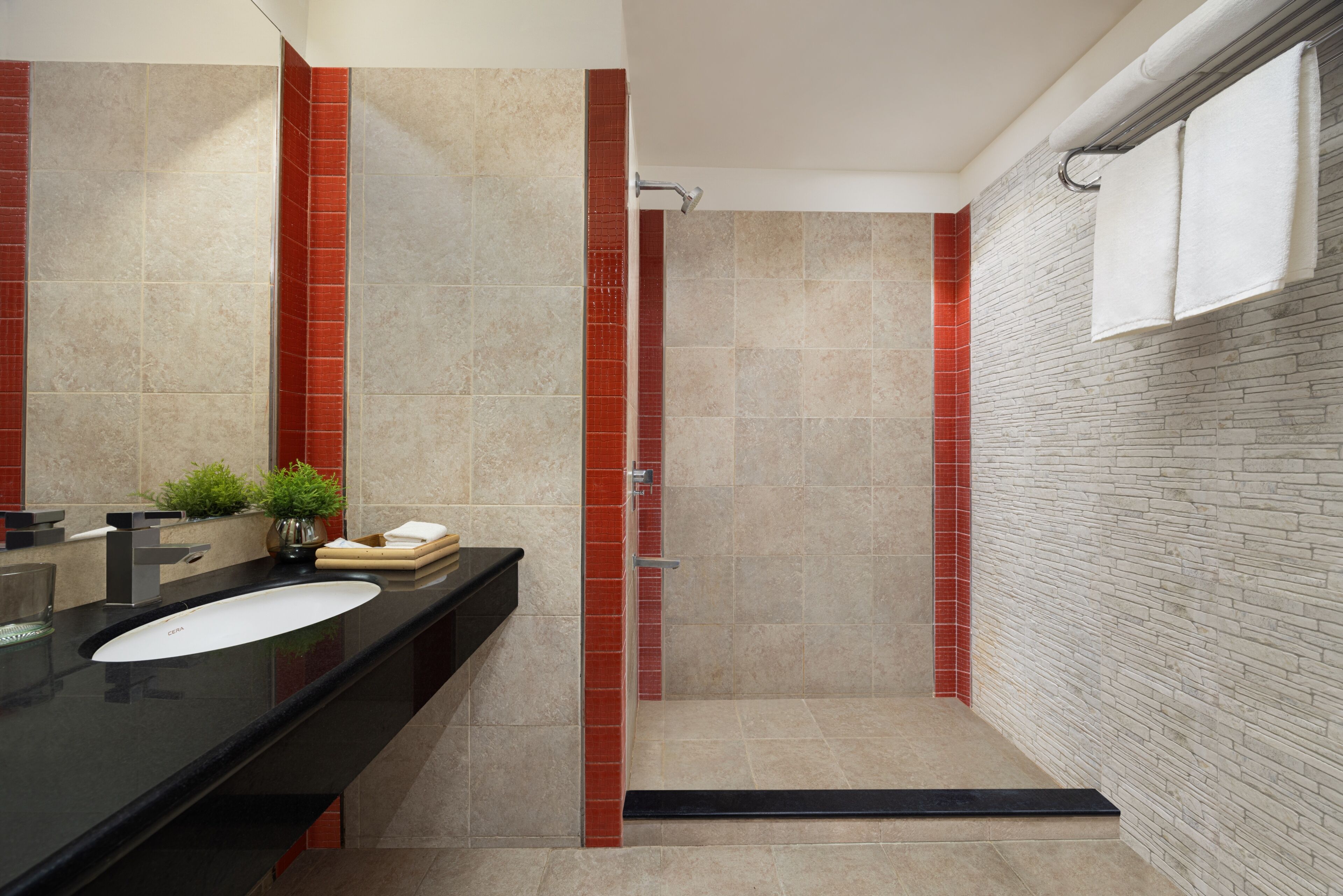 A modern bathroom with a black countertop, a white sink, a shower with a glass door, and a brick-patterned wall.